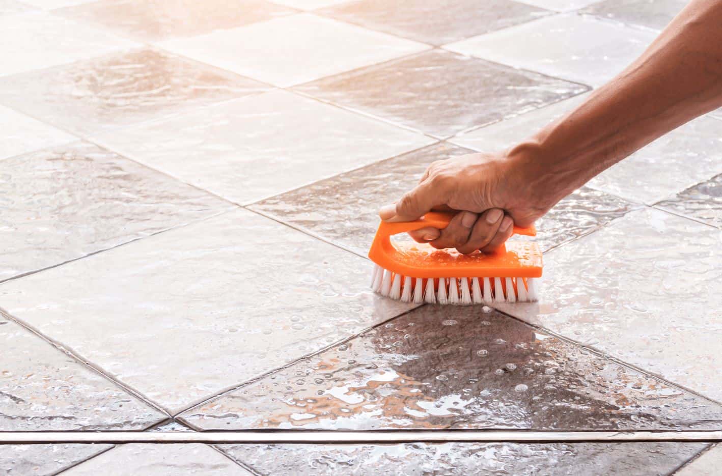 man using orange bristled brush to clean natural stone tile
