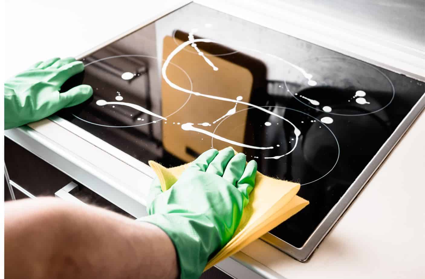 man wearing green gloves degreasing a black 4 burner induction cooktop
