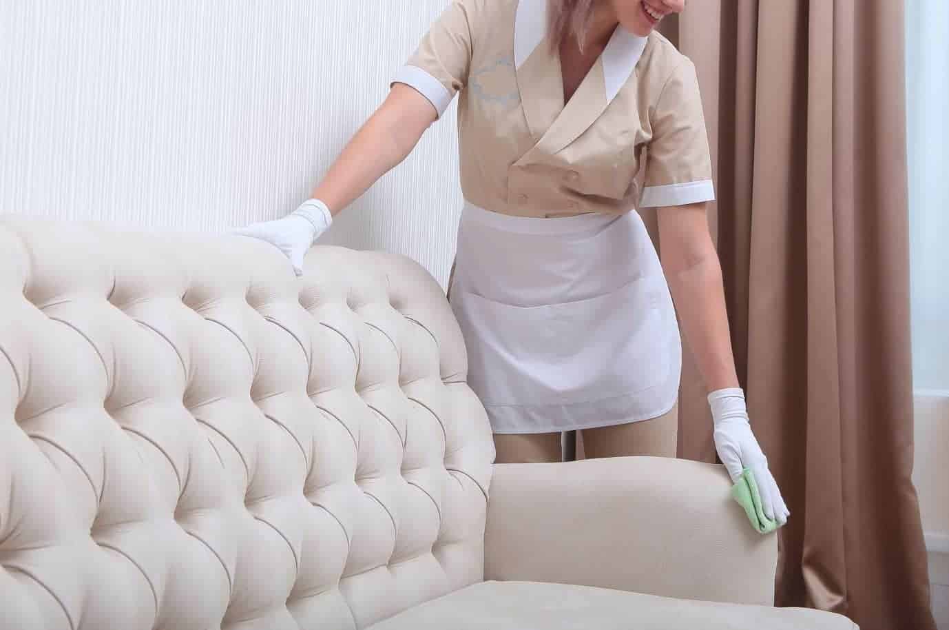 woman wiping down white suede couch with green microfibre rag