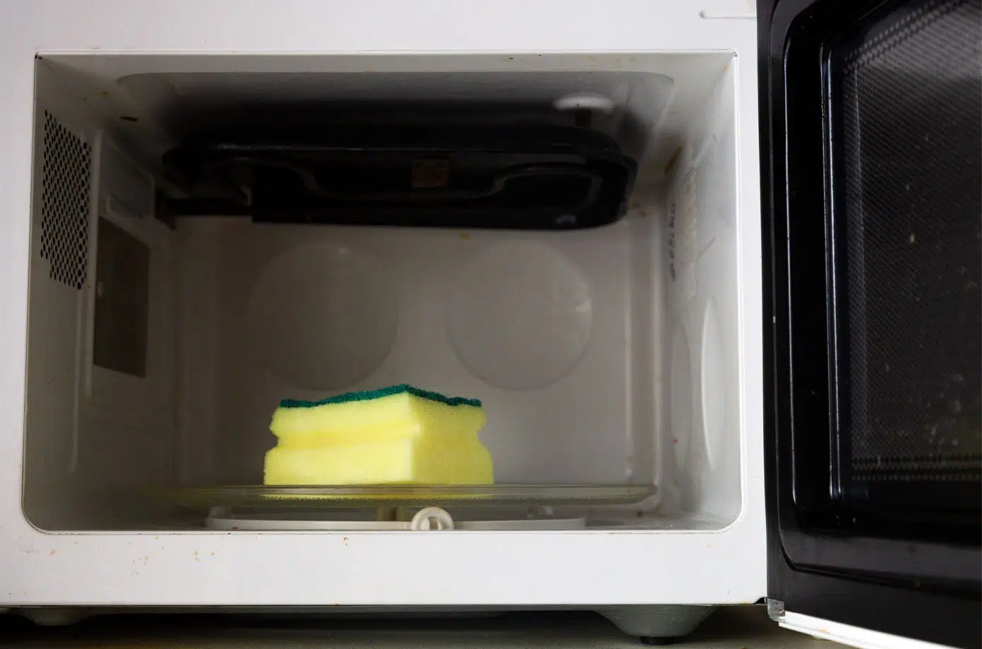 a yellow sponge on the dishtray of a dirty white microwave