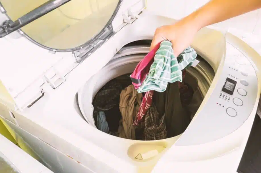 assorted clothes being put into a top loader washing machine
