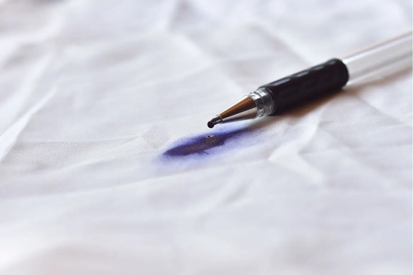 blue pen on its side dripping ink onto white fabric