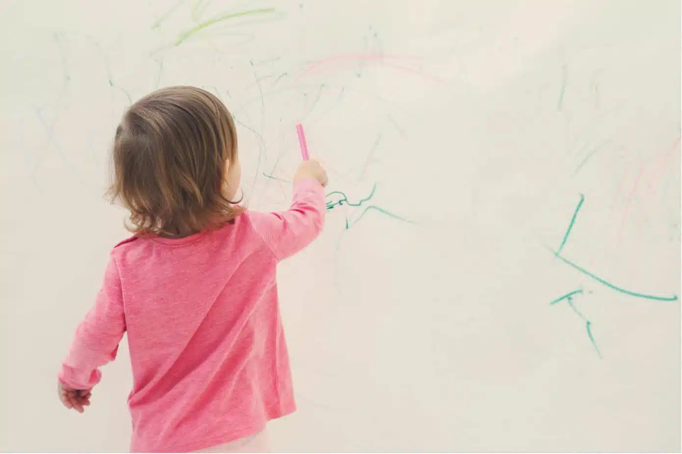 child drawing on a white painted wall with a crayon