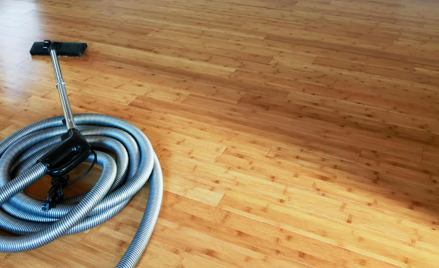 gray vacuum cleaner with black vacuum head on a large light brown bamboo floor