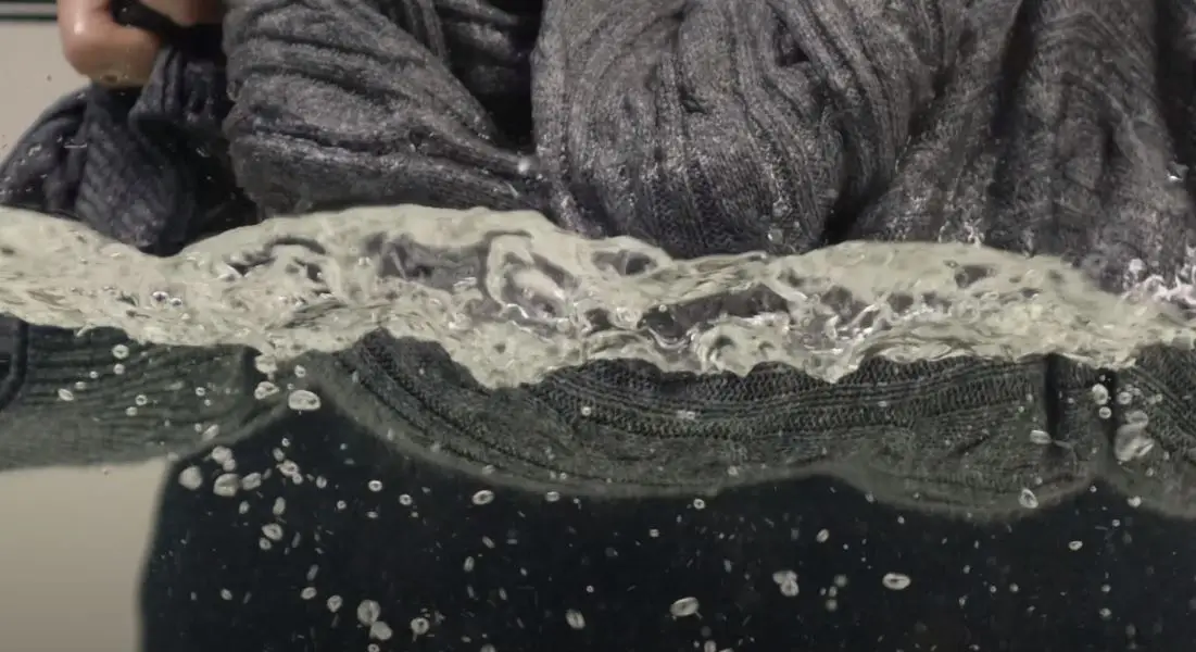 handwashed grey sweater being removed from large tub of water