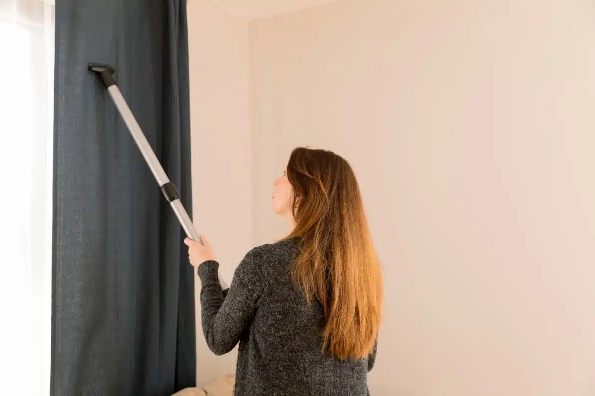 lady cleaning a blue hang down curtain with a vacuum