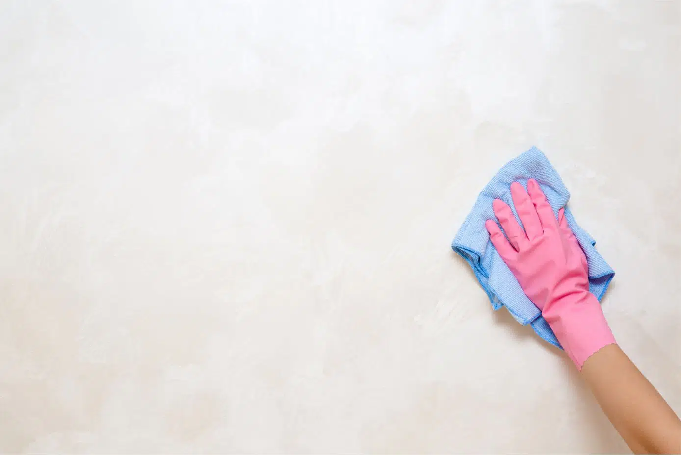 person wearing pink gloves wiping wall with a blue microfiber cloth