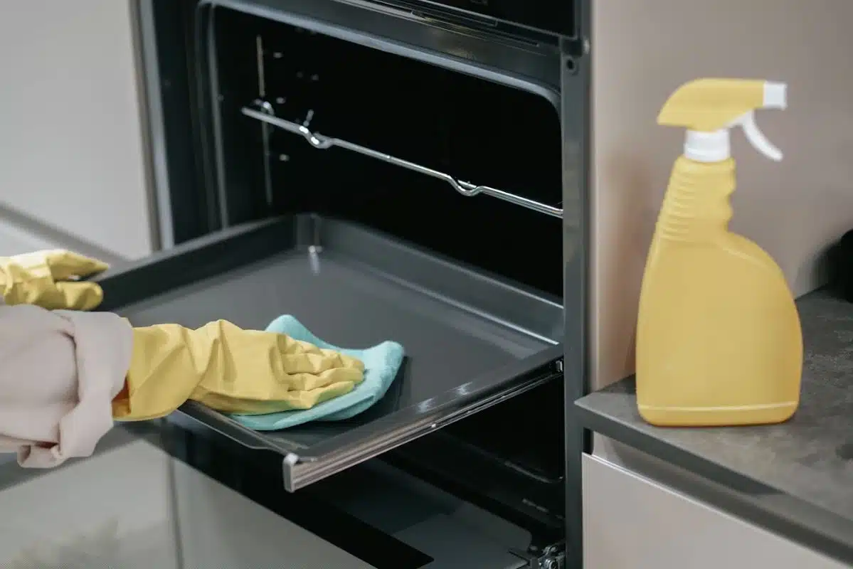 person wearing yellow gloves cleaning oven trays with a blue cloth