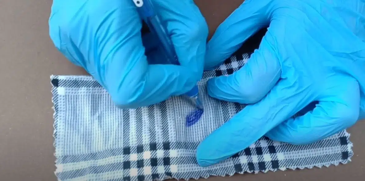 person with blue rubber gloves writing with a blue pen on a black and white cotton cloth