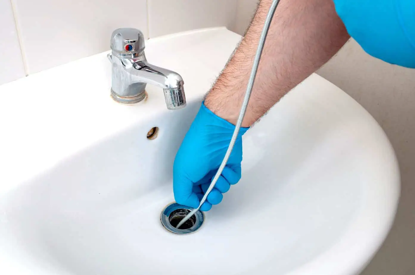 plumber wearing blug gloves fixing a drain with a plumbers snake