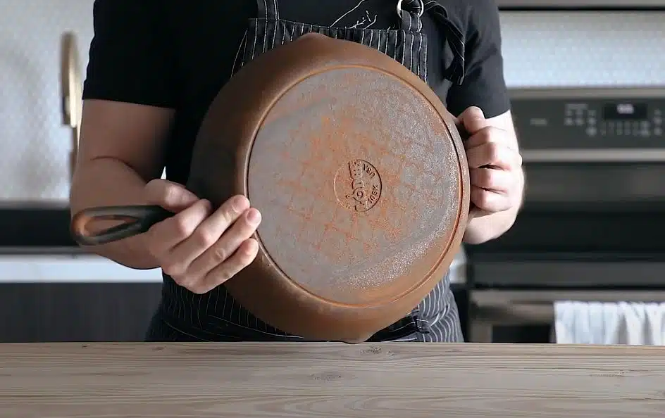 A rusted cast iron skillet being held up by a chef
