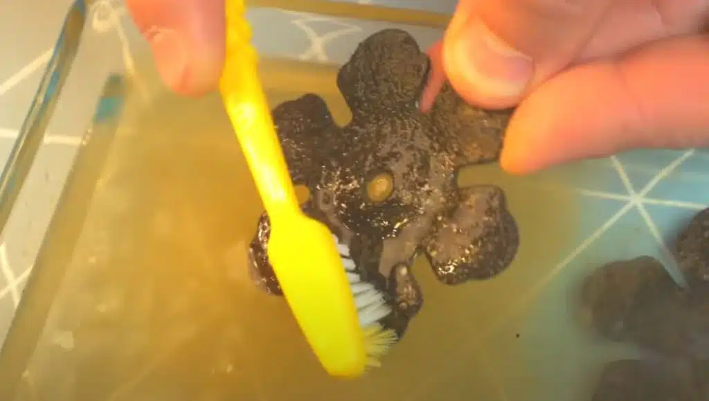 rusted ornament being cleaned by a yellow toothbrush