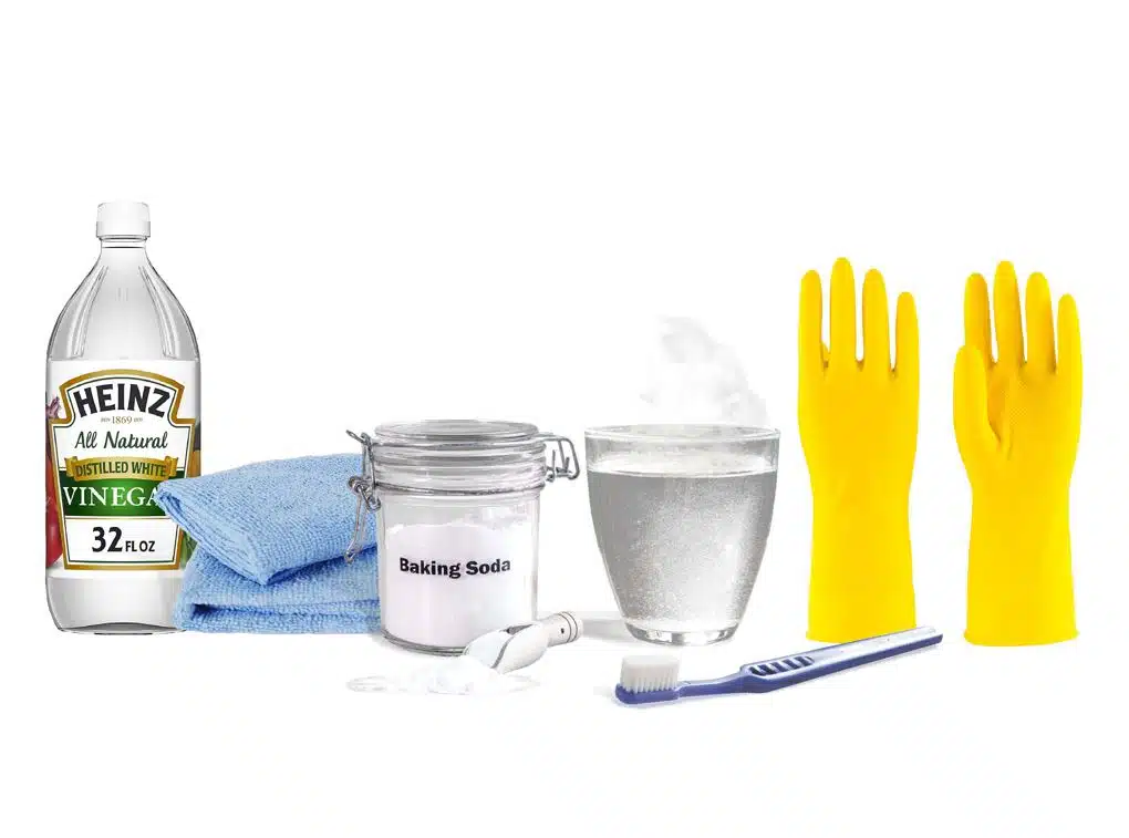 vinegar, blue microfibre cloths, baking soda, yellow gloves and a blue toothbrush on a white background