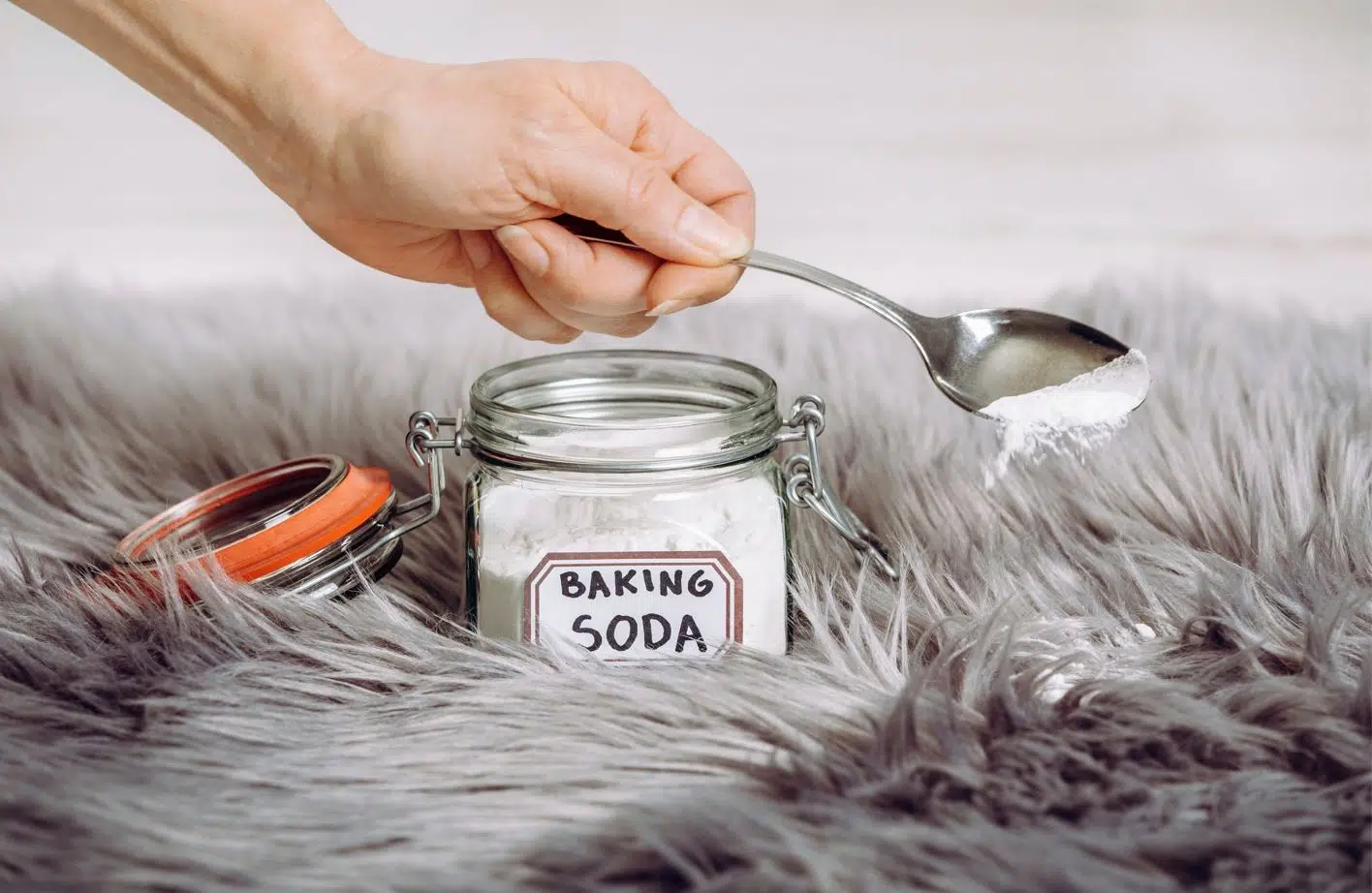 woman sprinkling a tablespoon of baking soda onto a grey shagged carpet