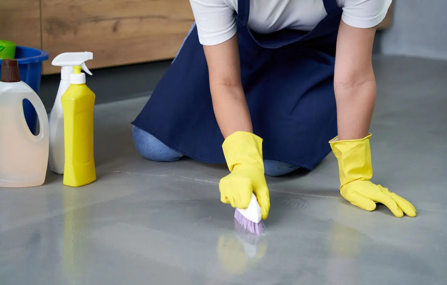 woman wearing blue apron and yellow rubber gloves scrubbing a gray porcelain floor